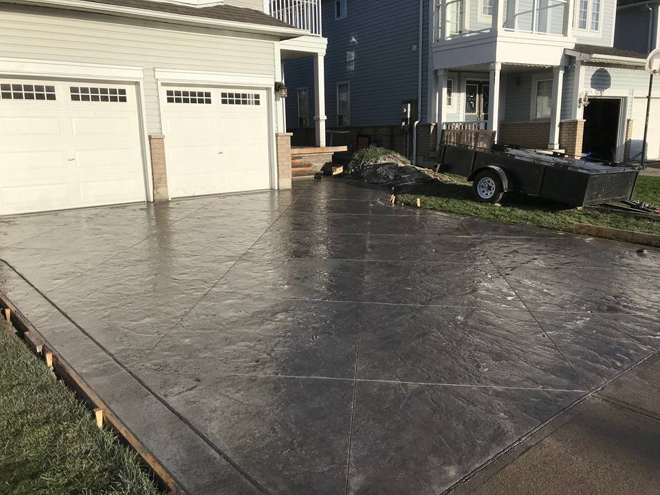 Large dark stamped tile driveway freshly poured at dusk, forms in place