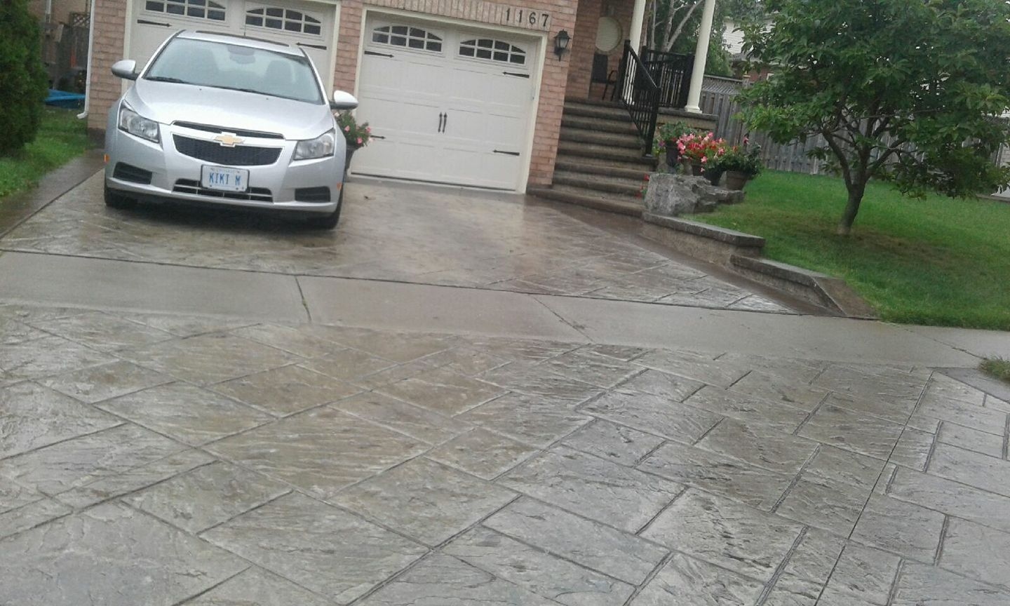 Grey stamped tile driveway glistening in the rain with curved front walkway