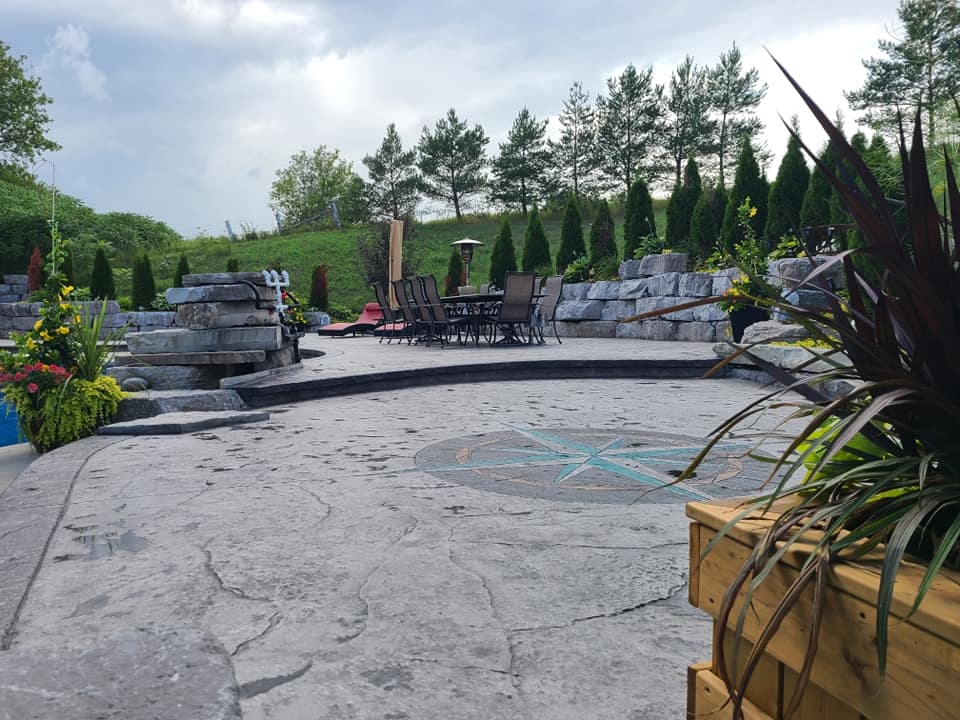 Large decorative stamped patio with compass rose inlay, outdoor dining, and stone walls