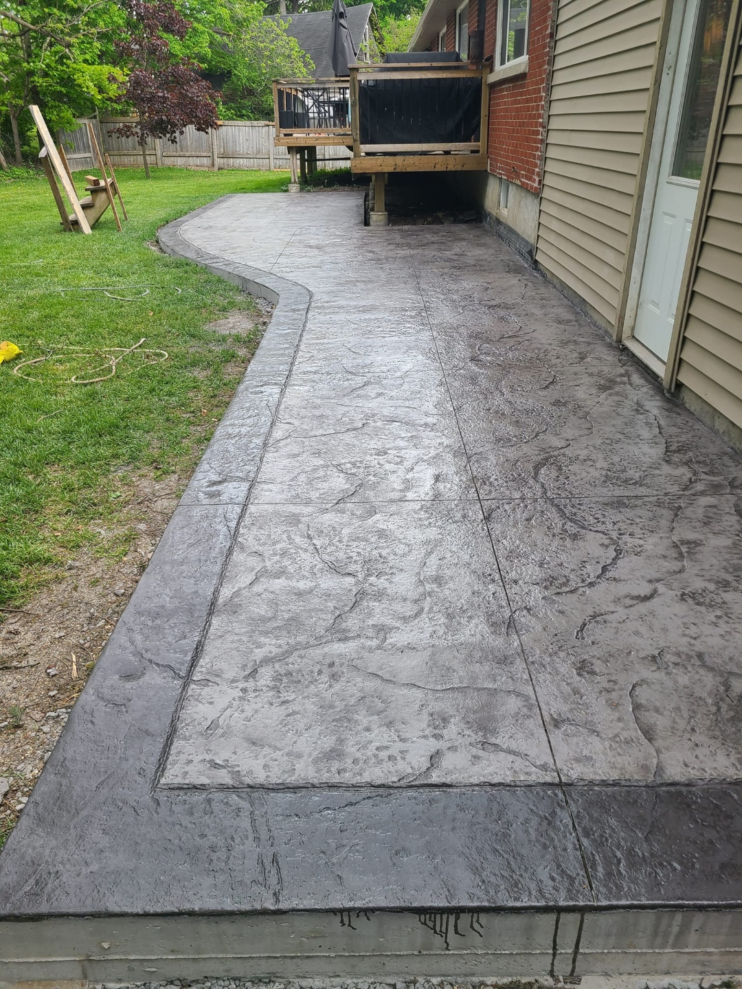 Long grey flagstone-stamped concrete patio beside house