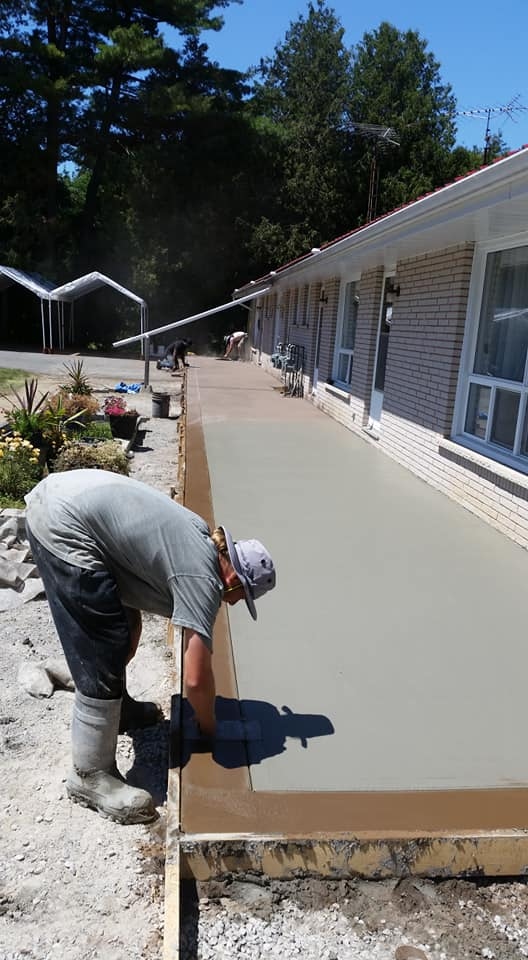 Crew finishing long concrete slab pour beside bungalow home