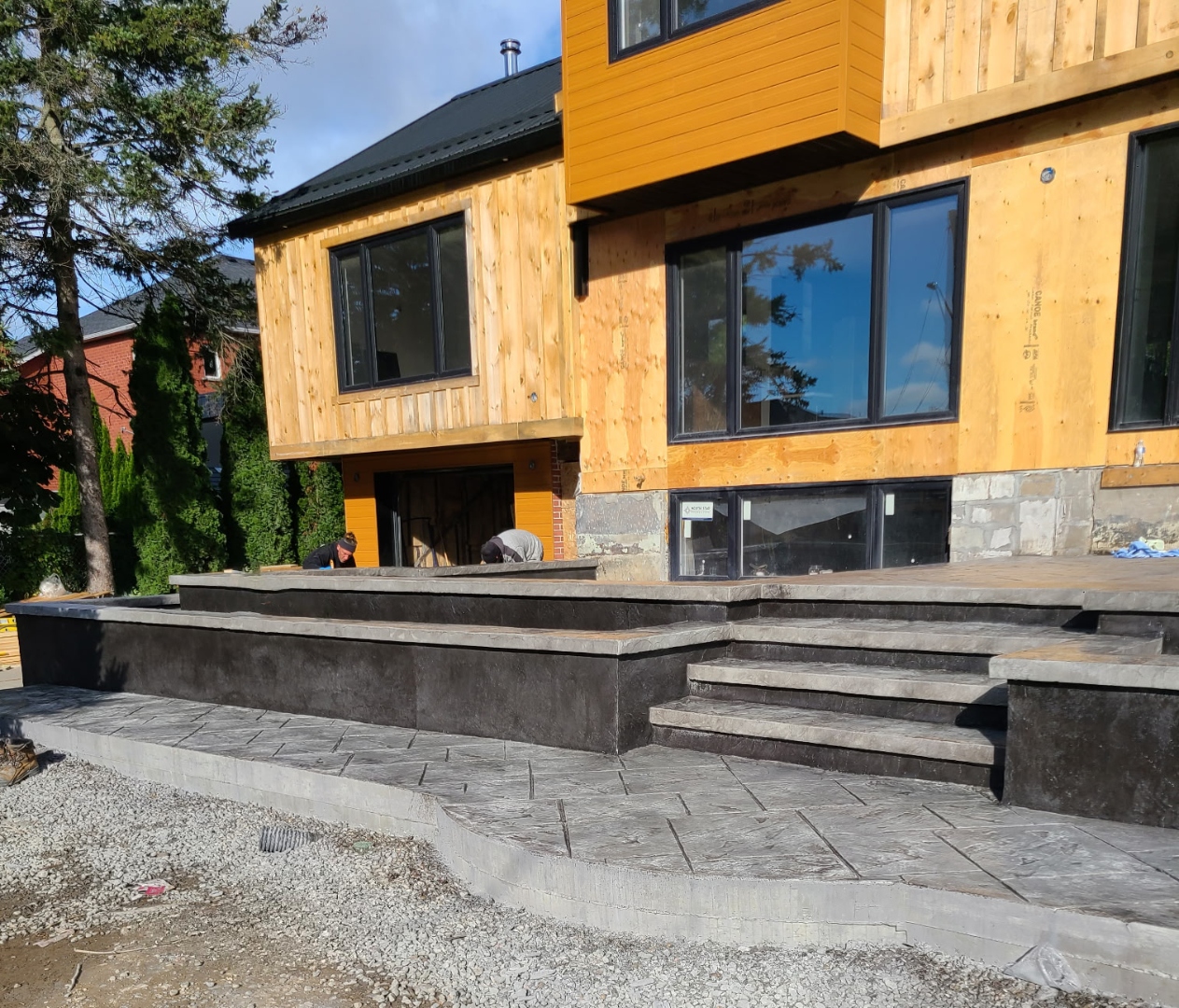 Wide view of stamped patio and stairs on modern home, crew working