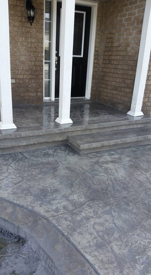 Freshly sealed grey stamped concrete front porch with steps and white columns