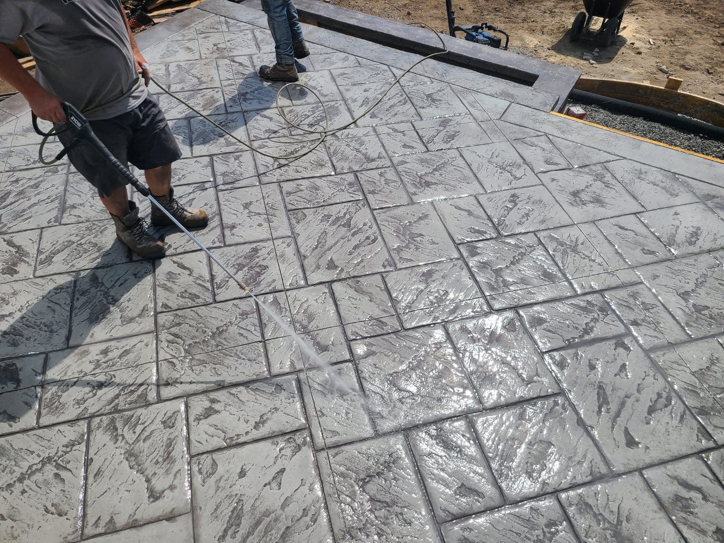 Crew pressure-washing freshly stamped large tile patio