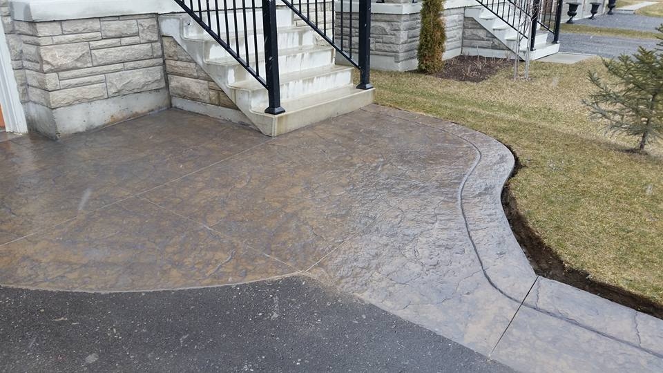 Curved stamped walkway and entrance pad beside elegant stone home with iron railings