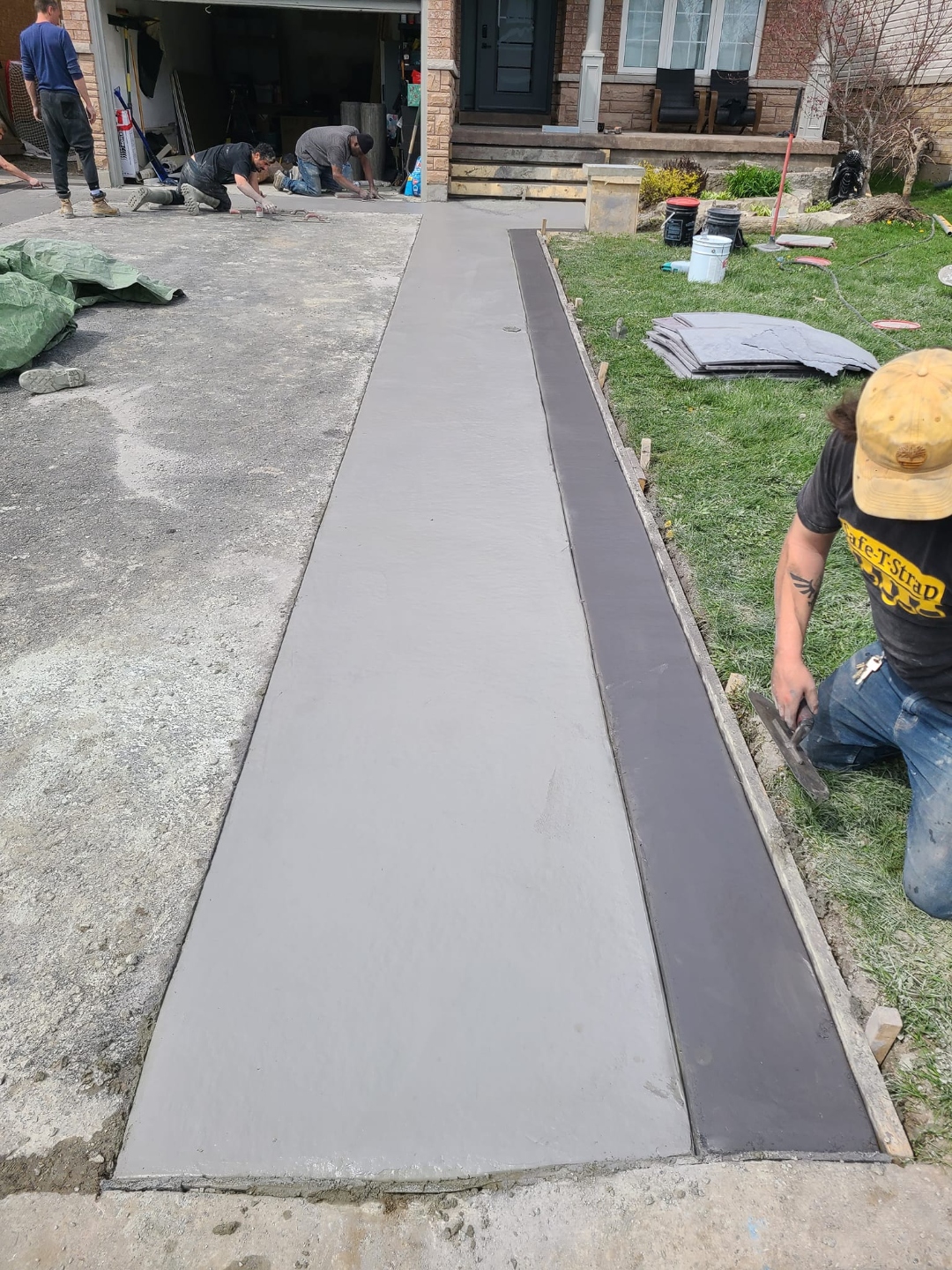 Crew finishing fresh concrete walkway pour beside home